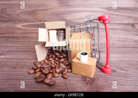 Chariot à provisions miniature renversé avec boîtes d'expédition de jouets avec grains de café torréfiés et tasses isolées sur un fond en bois. Banque D'Images