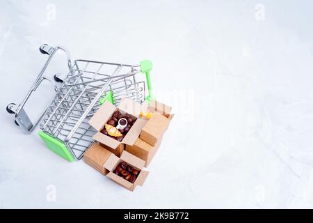 Lot de petites boîtes d'expédition avec des grains de café torréfiés et des croissants par un petit chariot à provisions renversé isolé sur fond gris avec cop Banque D'Images