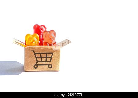 Bonbons à l'ours en gelée colorés dans une petite boîte d'expédition étiquetée avec un symbole de chariot de poussée isolé sur fond blanc. Banque D'Images