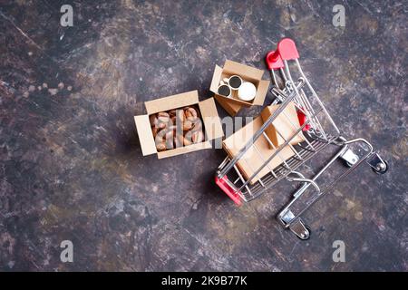 Chariot de poussée miniature renversé avec boîtes d'expédition minuscules avec grains de café torréfiés et tasses à café jetables. Banque D'Images