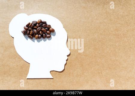 Coupe de papier à profil de tête femelle avec grains torréfiés isolés sur fond marron. Concept créatif de dépendance à la caféine. Banque D'Images