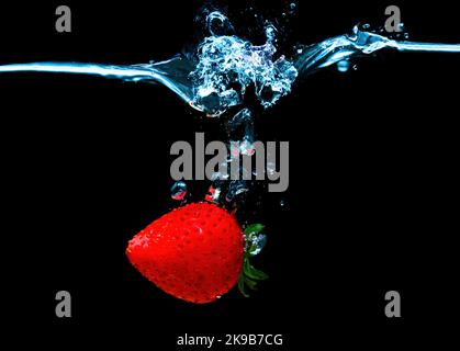 Fraise mûre entière unique, coulant sous l'eau avec des éclaboussures isolées sur fond noir. Banque D'Images