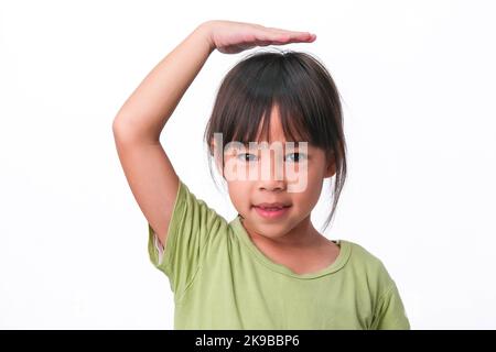 Petite fille souriante montrant ses dents cassées et mettant sa main sur sa tête montrant la croissance, isolée sur fond blanc. Banque D'Images