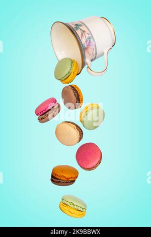 Des macarons volants tombant d'une coupe vintage sur fond bleu Banque D'Images