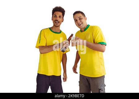 Black Brothers avec jaune Brazilian shirt et bouteille de bière acclamations isolats sur blanc. Les fans de football applaudissent pour que le Brésil soit le champion. Banque D'Images