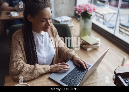 Jeune femme afro-américaine élégante et attrayante utilisant un ordinateur portable au café Banque D'Images