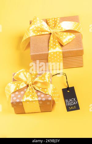 Deux boîtes-cadeaux en papier kraft avec rubans et noeuds jaunes à pois sur fond jaune et étiquette DE SOLDE NOIRE LE VENDREDI. Concept de vente festive. Banque D'Images