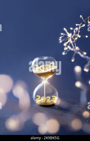 Fin de l'année 2022, Silverster, bonne année 2023. HourGlass avec les numéros 2022 et 2023 et guirlande claire sur fond bleu foncé. HourGlass est Banque D'Images