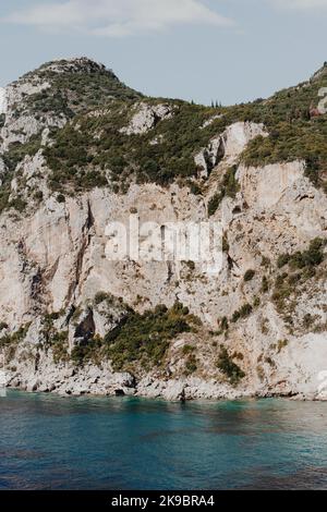 Corfou, Grèce.Un immense rocher de montagne sur lequel les plantes vertes poussent par belle eau bleue où le soleil d'été brille. Banque D'Images