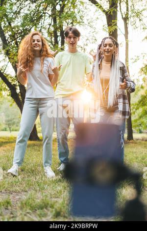 Portrait d'adolescents positifs filmant tutoriel de danse vidéo tendance pour les réseaux sociaux dans le parc de la ville au coucher du soleil. Amitié multiethnique. Été Banque D'Images