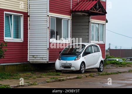 Yuzhno-Kurilsk, Russie - 02 août 2022: Voiture électrique sous-compacte Mitsubishi i-MiEV près d'une ancienne maison dans un village balnéaire Banque D'Images