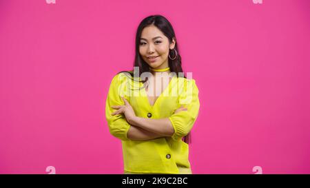 jolie femme asiatique debout avec des bras croisés isolée sur rose Banque D'Images