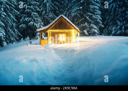 Paysage d'hiver fantastique avec cabine en bois lumineux dans une forêt enneigée. Maison confortable dans les montagnes de Carpathian. Concept de vacances de Noël Banque D'Images