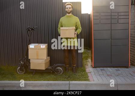 Homme debout avec une caisse près du terminal de poste automatique et du scooter Banque D'Images