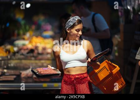 Une jeune femme choisit de la viande dans une épicerie Banque D'Images