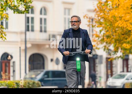 Homme d'âge moyen avec cheveux gris et barbe portant des vêtements élégants sur location de scooter électrique dans le centre-ville. Prise de vue horizontale en extérieur. Photo de haute qualité Banque D'Images