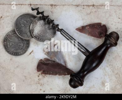 Collection vintage unique de tire-bouchon antique, de pointes de flèches amérindiennes et de pièces en argent sur fond de papier fondu en gros plan Banque D'Images