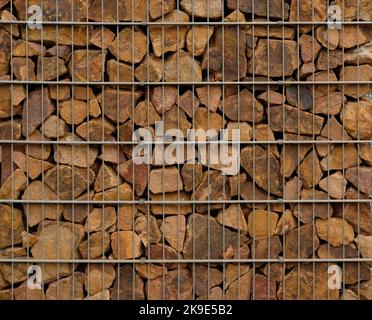 Mur de soutènement de gabion - gros plan de pierres brunes dans des paniers métalliques de gabion maintenus par un mur de soutènement. Banque D'Images