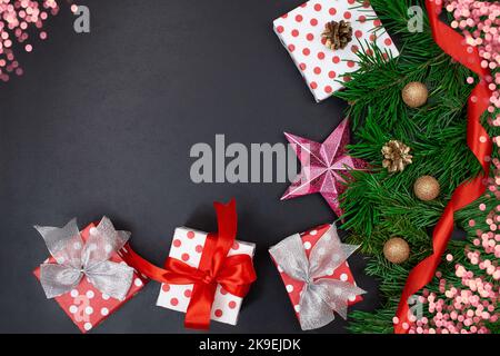 Boîtes-cadeaux avec arcs, branches de sapin, étoile, ruban et bokeh sur fond noir. Noël, nouvel an. Copier l'espace Banque D'Images