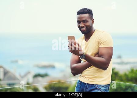 Un beau jeune homme qui utilise son téléphone portable tout en se relaxant en plein air pendant ses vacances, vérifie ce que les médias sociaux sont à la hauteur de ces vacances. Banque D'Images