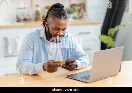 Afro-américain homme faisant des achats en ligne à la maison en utilisant ordinateur portable et carte de crédit, banque en ligne Banque D'Images
