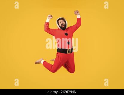 Photo de corps pleine longueur d'homme sautant avec bonheur vêtu du costume du père noël sur fond jaune, bonheur du nouvel an Banque D'Images