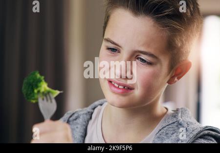 Pourquoi les légumes ne peuvent pas avoir le goût de bonbons. Un jeune garçon refuse de manger son brocoli à la maison. Banque D'Images