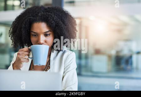 Concentré et prêt à livrer. Une jeune femme d'affaires ayant une tasse de café tout en faisant un peu de travail à son bureau. Banque D'Images