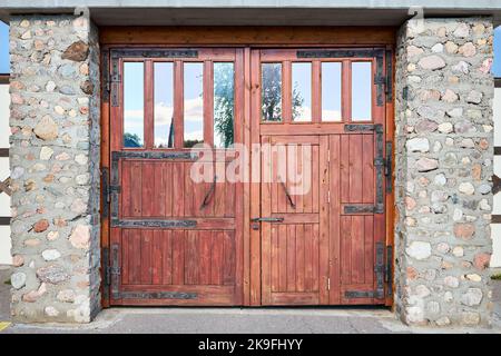 Anciennes grandes portes en bois dur texturées, vieux mur en brique avec de grandes portes anciennes stables s'accouple à la forge avec des éléments de montage forgés. Porte de grange en bois Banque D'Images