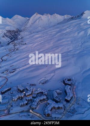 Vue aérienne des chalets de village de montagne illuminés par des lumières de rue de nuit le long des routes sinueuses à la lumière du crépuscule au coucher du soleil. Station de ski avec neige Banque D'Images