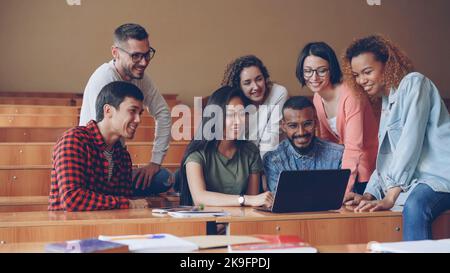 Un groupe d'étudiants participe à une visioconférence à l'aide d'un ordinateur portable, ils regardent l'écran en agitant les mains, en souriant et en parlant. Technologie moderne et concept d'éducation. Banque D'Images