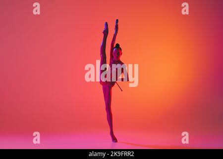 Belle et souple gracieuse athlète rythmique artiste de gymnastique danse, faisant des exercices d'étirement isolés sur fond coloré au néon. Beauté Banque D'Images