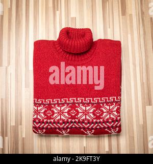 Pull de Noël tricoté rouge à col roulé de conception traditionnelle avec ornement géométrique scandinave blanc (alias Ugly Sweater) posé plié sur une bette en bois Banque D'Images