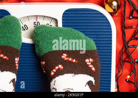 Une femme en chaussettes de Noël se tient sur la balance, se pèse après la gourmandise pendant les vacances Banque D'Images