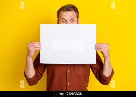 Photo d'intéressant garçon homme habillé élégant brun vêtements bras tenir feuille de papier couverture face vide espace isolé sur fond jaune Banque D'Images