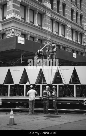 Une photo en échelle de gris des ouvriers de la construction soulevant un objet avec une grue dans le centre de New York Banque D'Images