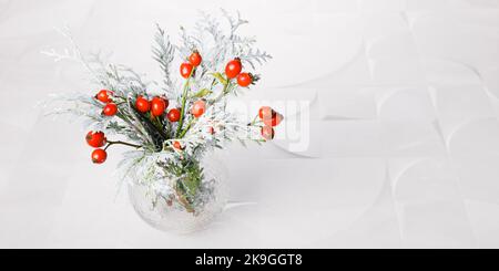 Bouquet d'hiver dans un vase en verre de branches de thuja dans la neige et de roses rouges sur fond de marbre Banque D'Images