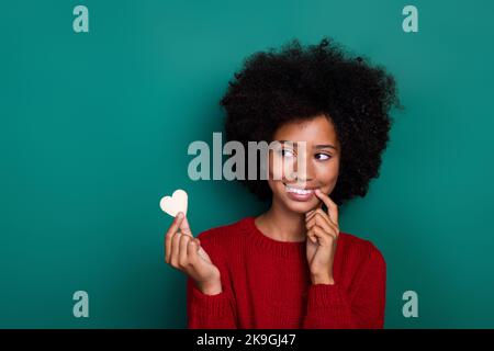 Photo de la charmante écolière look maintien coeur forme cookie morsure doigt habillé élégant rouge tricots ensemble isolé sur fond vert couleur Banque D'Images