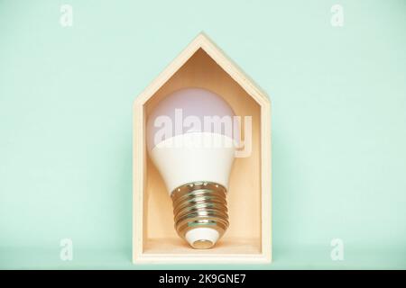 L'ampoule LED se trouve dans une petite maison en bois sur fond bleu, ce qui permet d'économiser de l'électricité dans la maison Banque D'Images