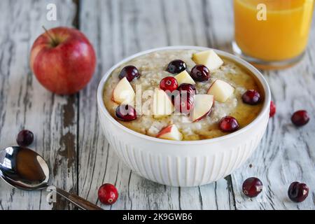 Bol chaud fait maison de flocons d'avoine crémeux à grains entiers avec pommes fraîches et canneberges entières. Mise au point sélective avec un premier plan et un arrière-plan flous. Banque D'Images