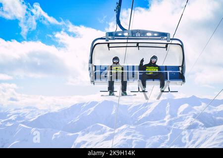 Gudauri, Géorgie - 25th mars 2022 : deux skieurs de patrouille de police s'assoient et font monter les pieds sur les remontées mécaniques de la station de ski de Gudauri. Aide à la sécurité et aux urgences Banque D'Images