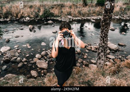 jeune fille caucasienne vêtue de vêtements de sport noirs prenant une photo regardant l'appareil photo à côté de pierres de rivière dans le tramway watawhata, nouvelle-zélande Banque D'Images