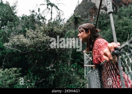 jeune femme caucasienne penchée sur la rampe métallique du long pont qui traverse la forêt et qui regarde malheureusement vers la rivière en donut Banque D'Images