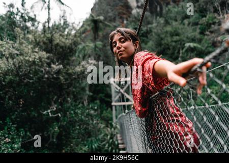 jeune femme caucasienne avec les yeux bleus veste rouge et les cheveux en forme de vaisselle penchée sur le pont de métal qui traverse la rivière regardant la caméra dans le donut Banque D'Images