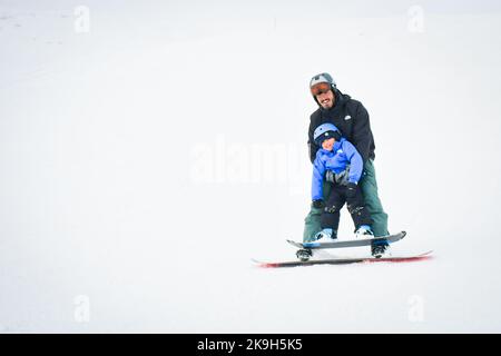 Gudauri, Géorgie - 25th mars, 2022: Père porter un petit garçon enfant sur le snowboard avoir le sourire amusant profiter de l'activité d'apprentissage. Vacances d'hiver en famille Banque D'Images