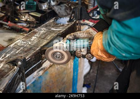 Homme travaillant avec une meuleuse angulaire rotative en atelier, gros plan sur les mains tenant l'outil Banque D'Images