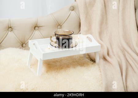 Plateau de petit déjeuner en bois blanc mignon avec pattes sur le lit de la maison avec une tasse de café chaud du matin, bougies allumées. Ensemble automne avec tissu écossais en laine douce. Banque D'Images