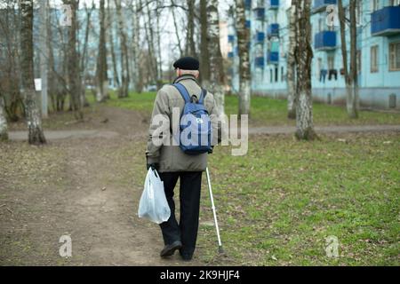 Un vieil homme marche dans la rue en été. Vieil homme avec un bâton de marche. L'homme marche dans le parc. Retour à la maison avec le sac à main. Banque D'Images