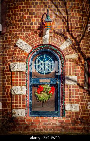 Porte voûtée dans une tourelle de maison en brique avec lumières de Noël et fenêtre ronde en vitraux et couronne de vacances Banque D'Images