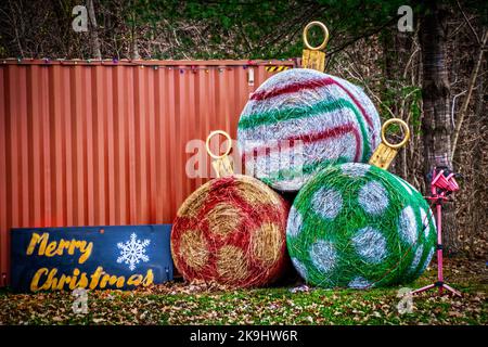 Campagne - scène rurale - grandes balles rondes de foin peintes comme des ornements de Noël avec signe de Joyeux Noël devant le wagon et les bois réaffectés - Banque D'Images